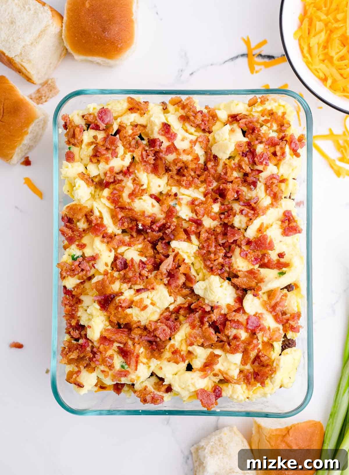 Morning Bites 14 Crumbled crispy bacon generously spread over the scrambled eggs layer in a glass baking dish, adding texture and flavor