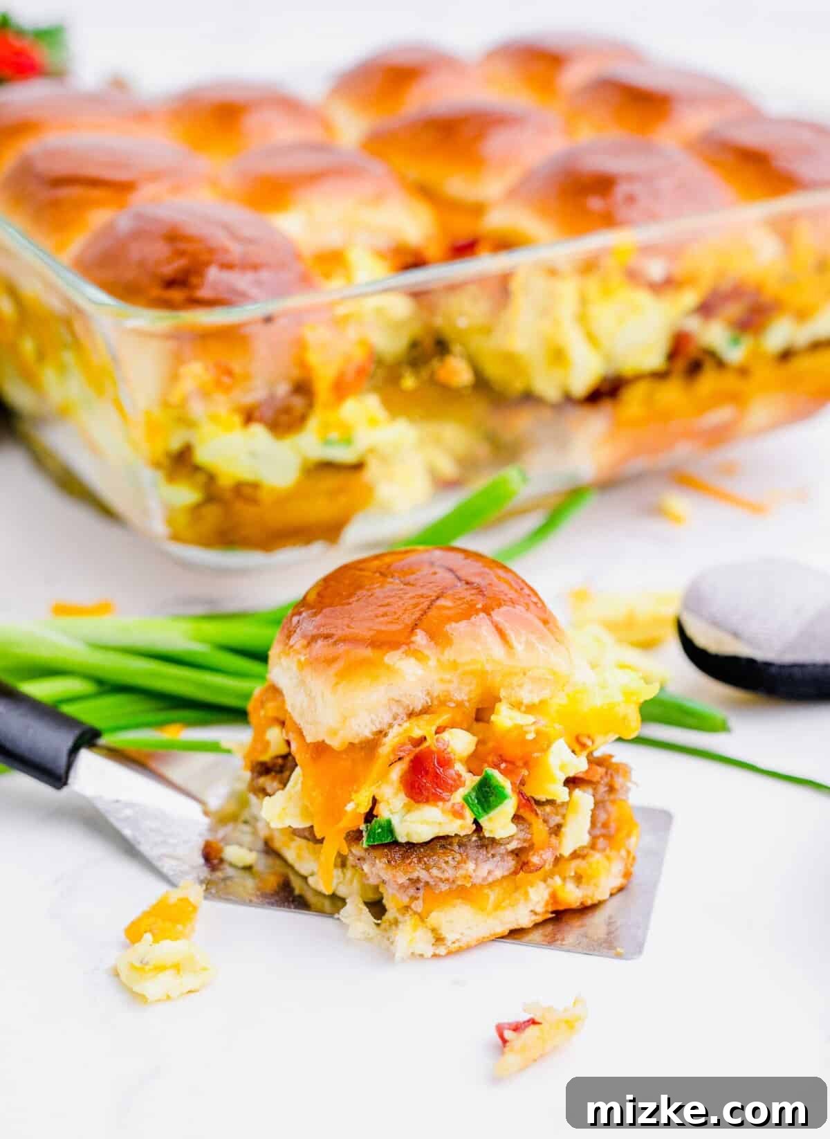 Morning Bites 17 A single breakfast slider on a spatula, ready to be served, with the baking dish filled with more sliders visible in the background