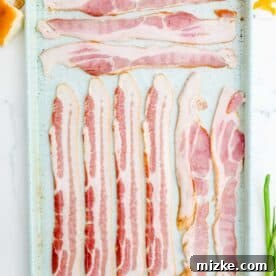 Bacon individually lined up on a metal baking sheet with parchment paper