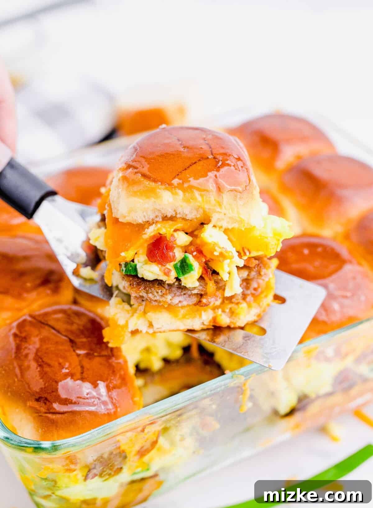 Morning Bites 4 One cheesy breakfast slider being carefully removed from a large baking dish with a spatula, ready to be served