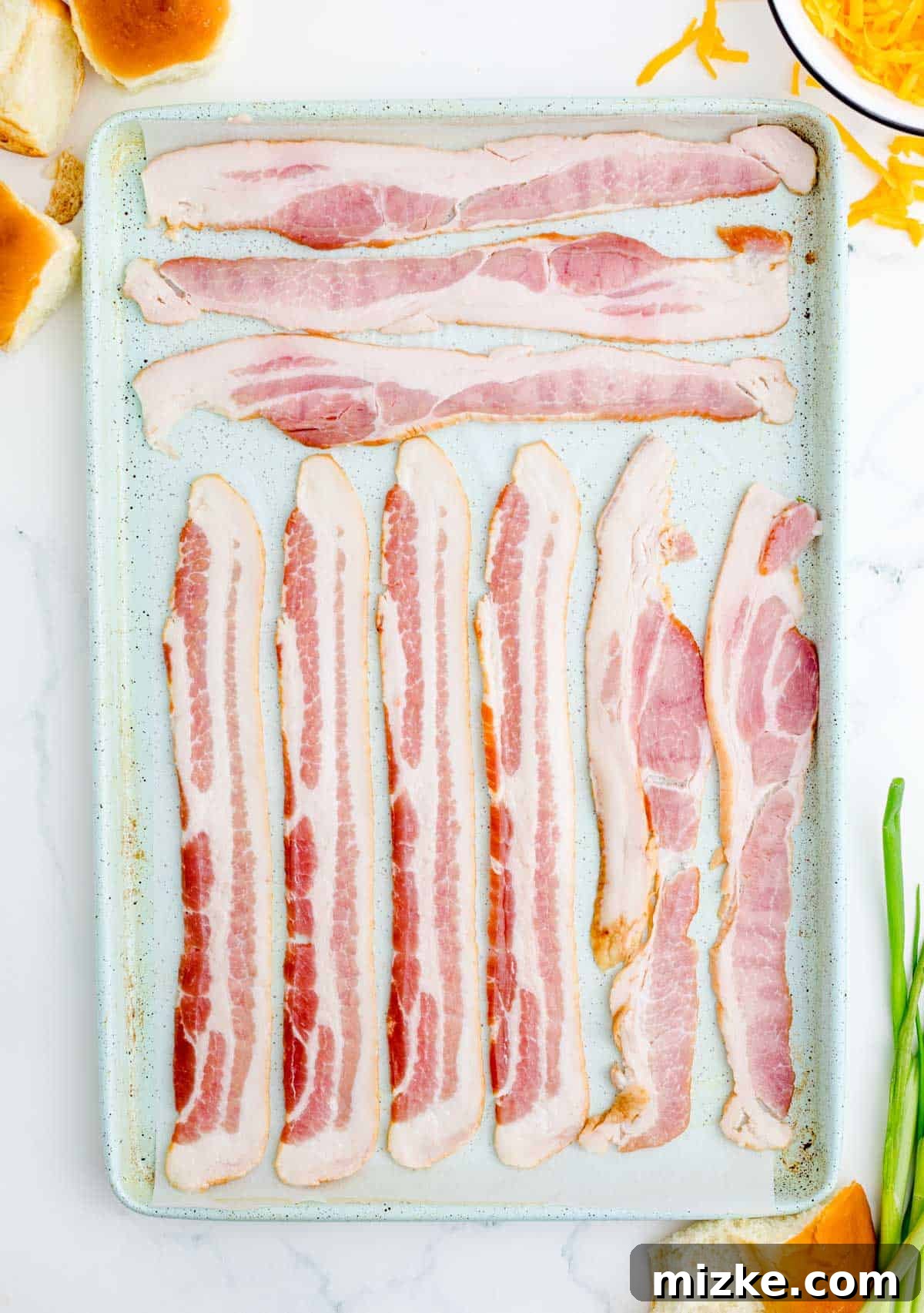 Morning Bites 7 Strips of uncooked bacon laid out neatly in a single layer on a metal baking sheet lined with parchment paper