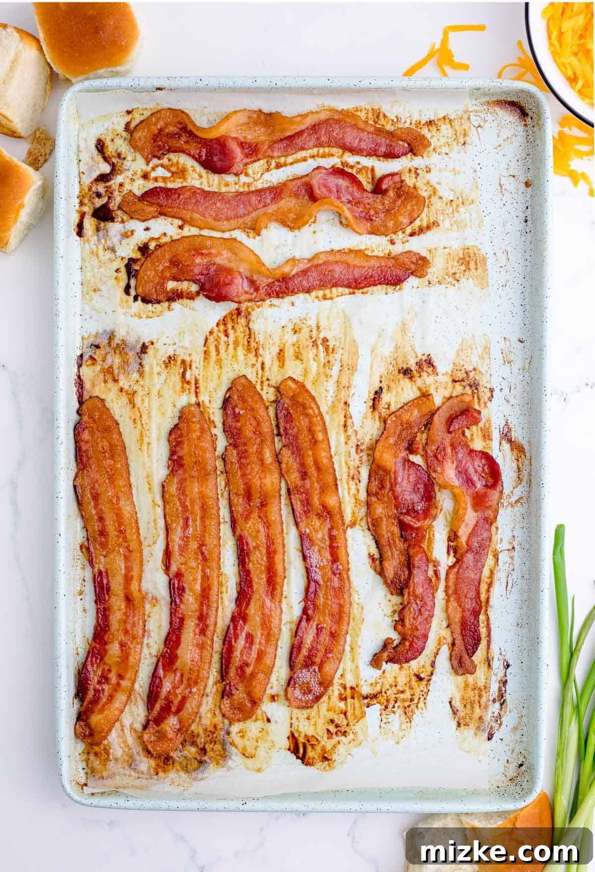 Morning Bites 8 Crispy, perfectly cooked bacon strips on a metal baking sheet, glistening after being baked