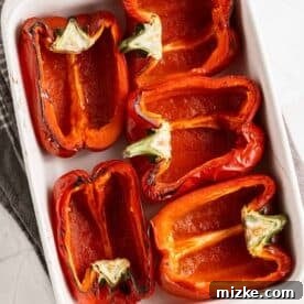 Red bell pepper halves meticulously arranged in a white baking dish, ready for roasting.