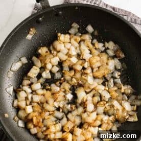 Finely diced onion and minced garlic sizzling gently in a nonstick black skillet, creating an aromatic base.