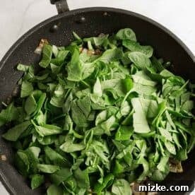 Fresh baby spinach leaves just added to the nonstick skillet, mixing with the fragrant garlic and onions.