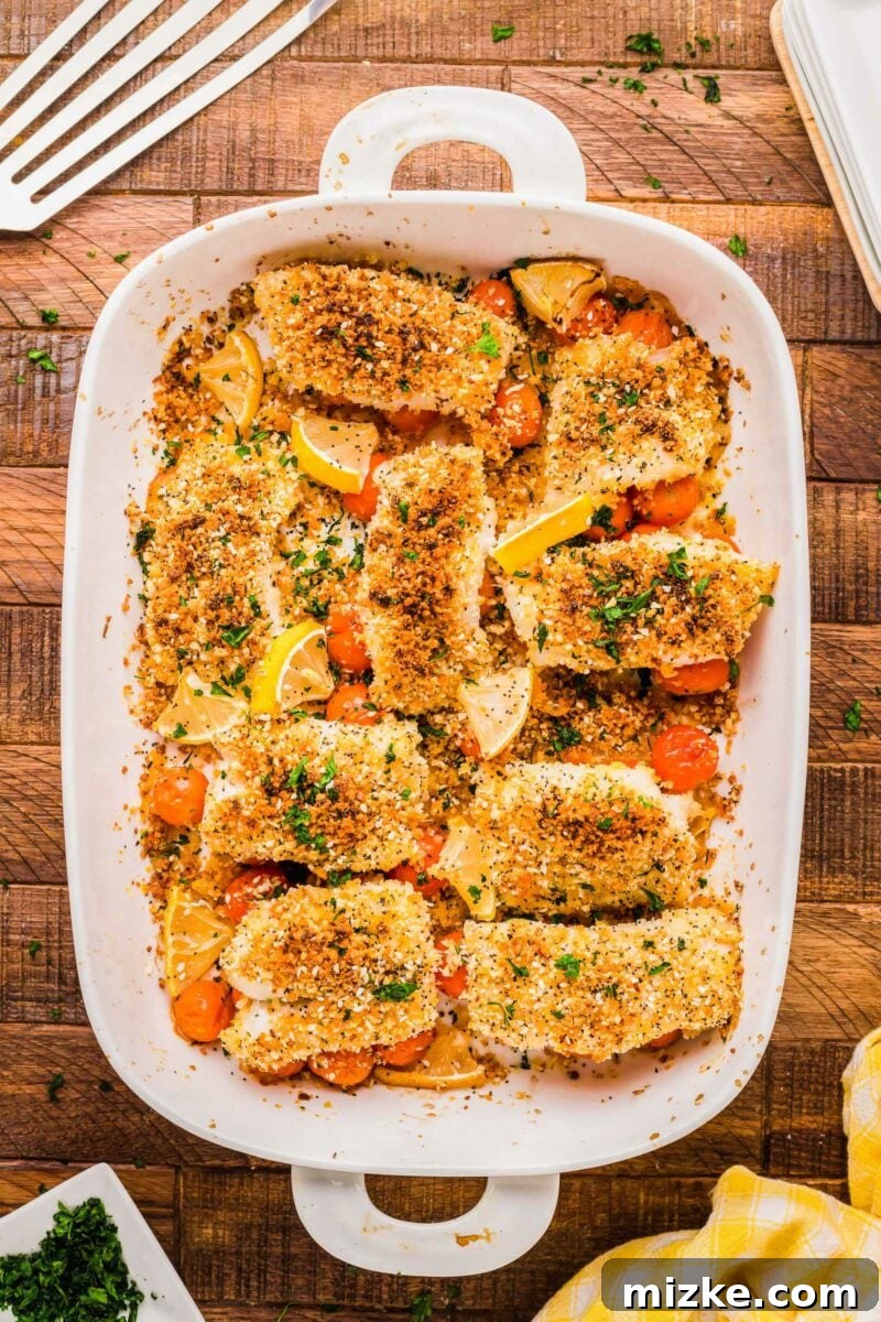 Crispy Everything Bagel Cod 2 A batch of baked cod filets is presented in a white baking dish, garnished with fresh herbs and lemon wedges.