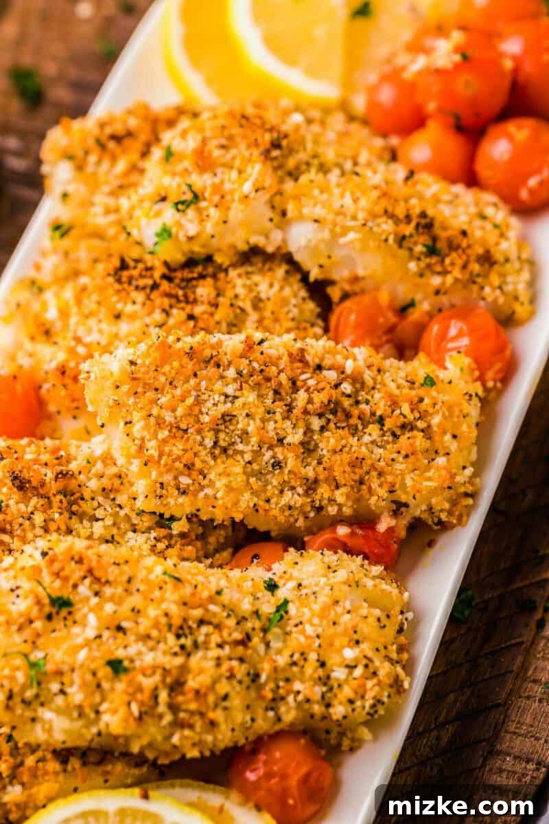 Crispy Everything Bagel Cod 4 Several crunchy pieces of baked cod are presented with baked cherry tomatoes on a white serving dish, garnished with fresh basil.
