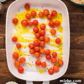Cherry tomatoes in a baking dish with olive oil and black pepper, ready for roasting alongside the cod.