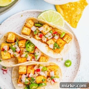 Three tofu tacos on plate with lime wedge and tortilla chips