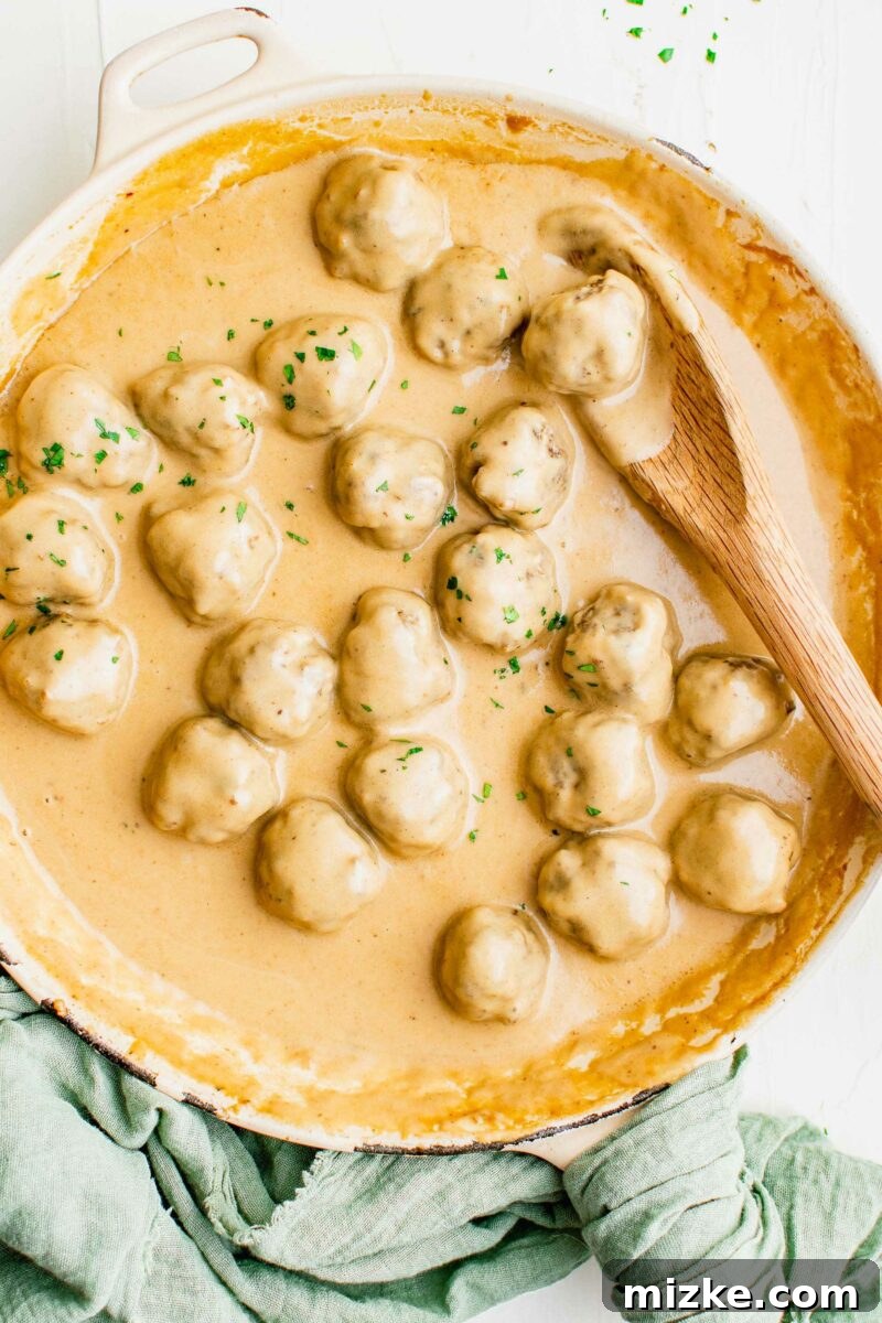 Irresistible Swedish Meatballs 2 A large pot brimming with perfectly cooked, tender meatballs generously coated in a luscious, light brown creamy sauce, ready to be served with a wooden spoon.