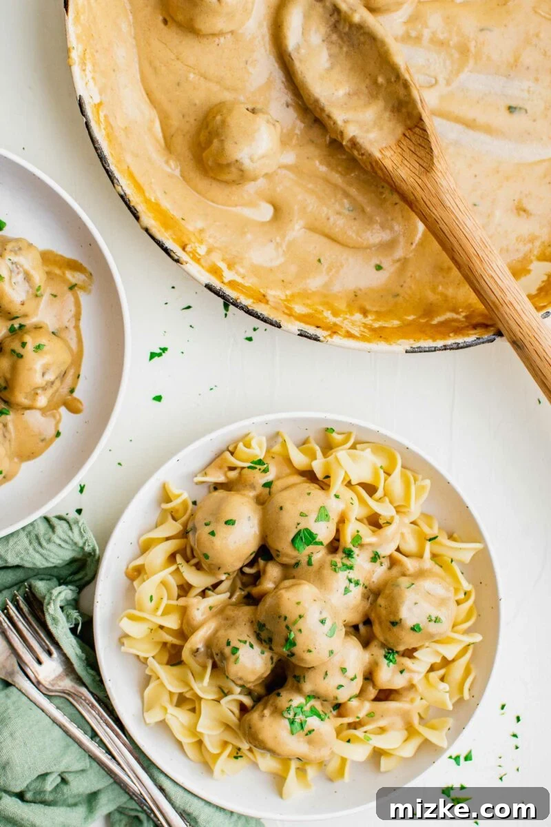 Irresistible Swedish Meatballs 3 A delectable serving of golden egg noodles on a crisp white plate, generously adorned with juicy Swedish meatballs and a sprinkle of vibrant fresh parsley, ready to be enjoyed.