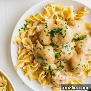 A close-up of a serving of Swedish meatballs with creamy sauce on a white plate, garnished with fresh parsley.