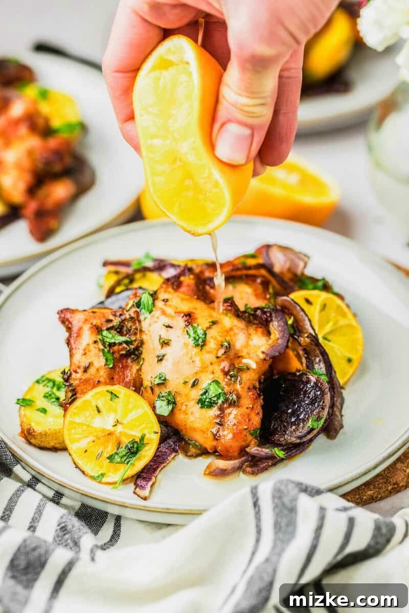 Zesty Meyer Lemon One-Pan Roasted Chicken 5 A fresh Meyer lemon being squeezed over a serving of cooked Meyer lemon sheet pan chicken on a pristine white plate, enhancing its fresh flavor.