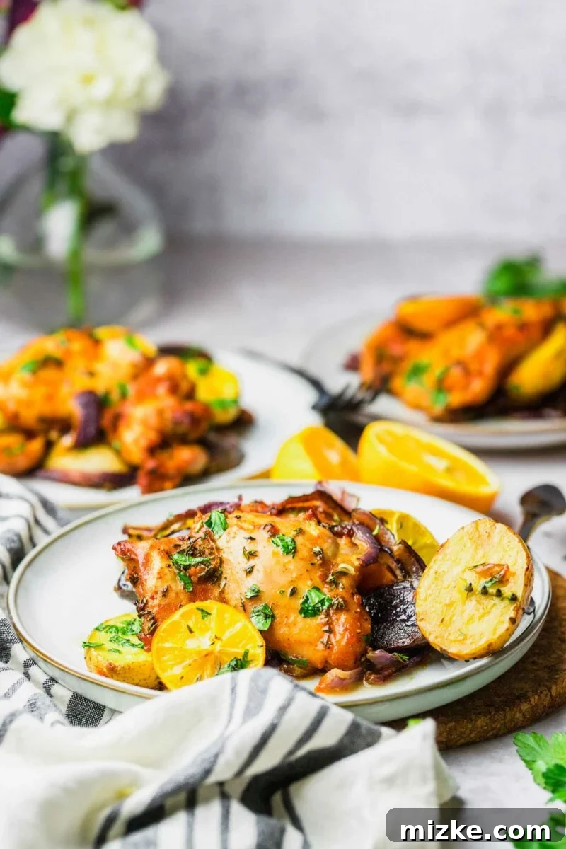 Zesty Meyer Lemon One-Pan Roasted Chicken 6 A close-up of tender roasted potatoes, sweet Meyer lemons, and succulent chicken thighs artfully arranged next to a fork on a white plate, highlighting the dish's texture and appeal.
