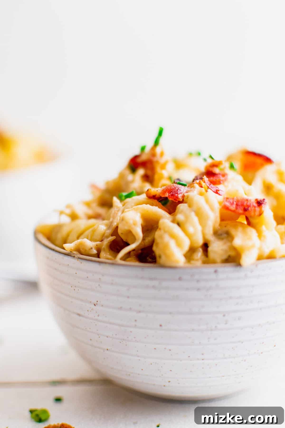 Bowl filled with crack chicken pasta, garnished with chives and bacon