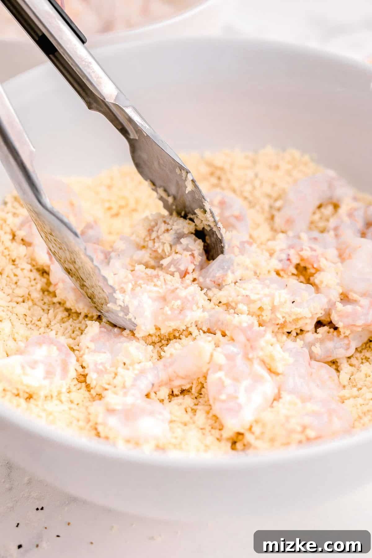 Dynamite Shrimp 8 adding the shrimp from the buttermilk mixture to the panko breadcrumbs mixture with silver tongs