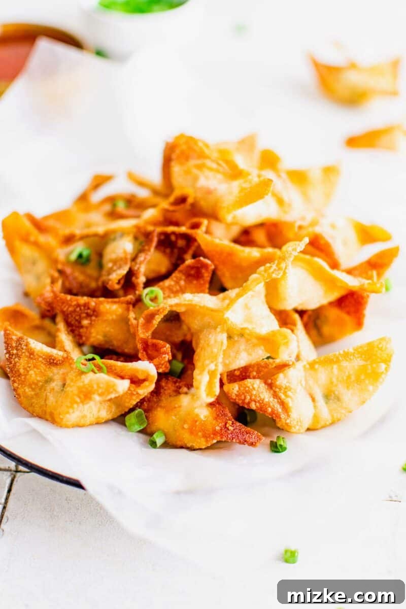 Golden Crispy Crab Bites 2 A stack of golden-brown crab rangoon are presented in a serving dish lined with parchment paper, garnished with fresh green onions.