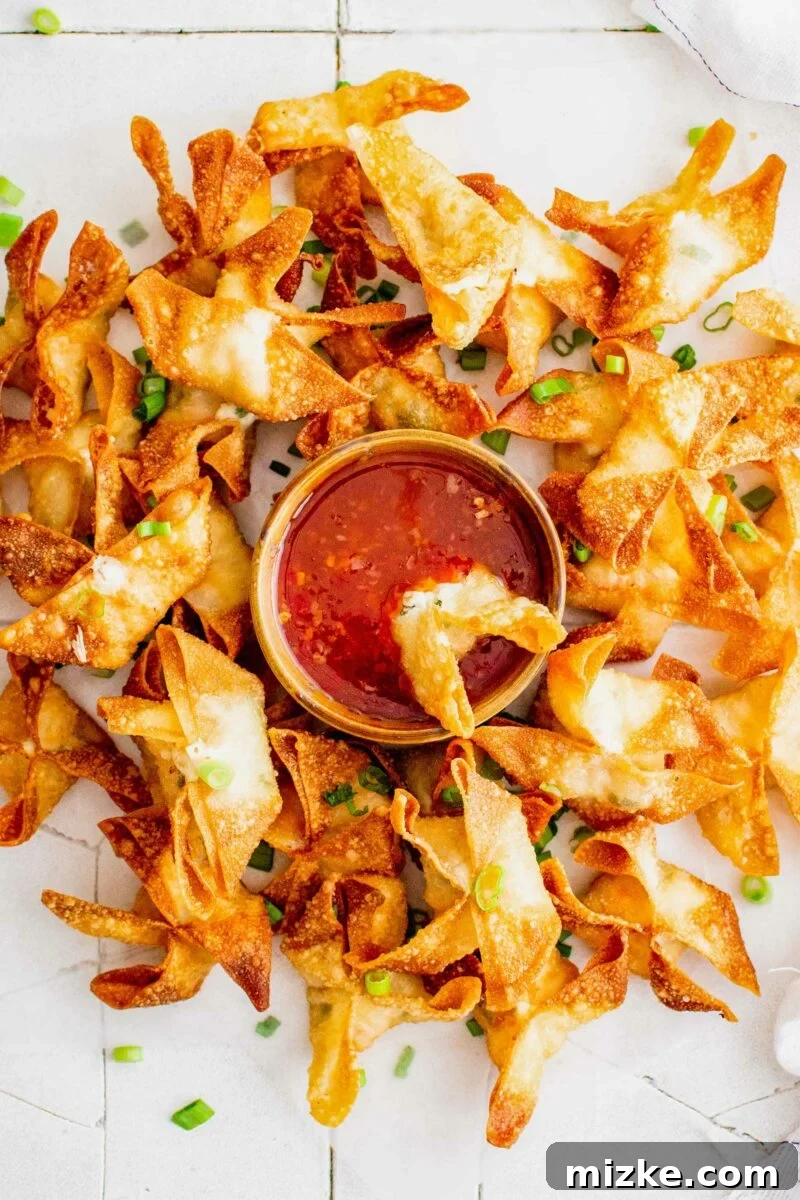 Golden Crispy Crab Bites 11 A crispy crab rangoon is being dipped into a small, elegant bowl of vibrant sweet chili sauce, highlighting its perfect pairing.