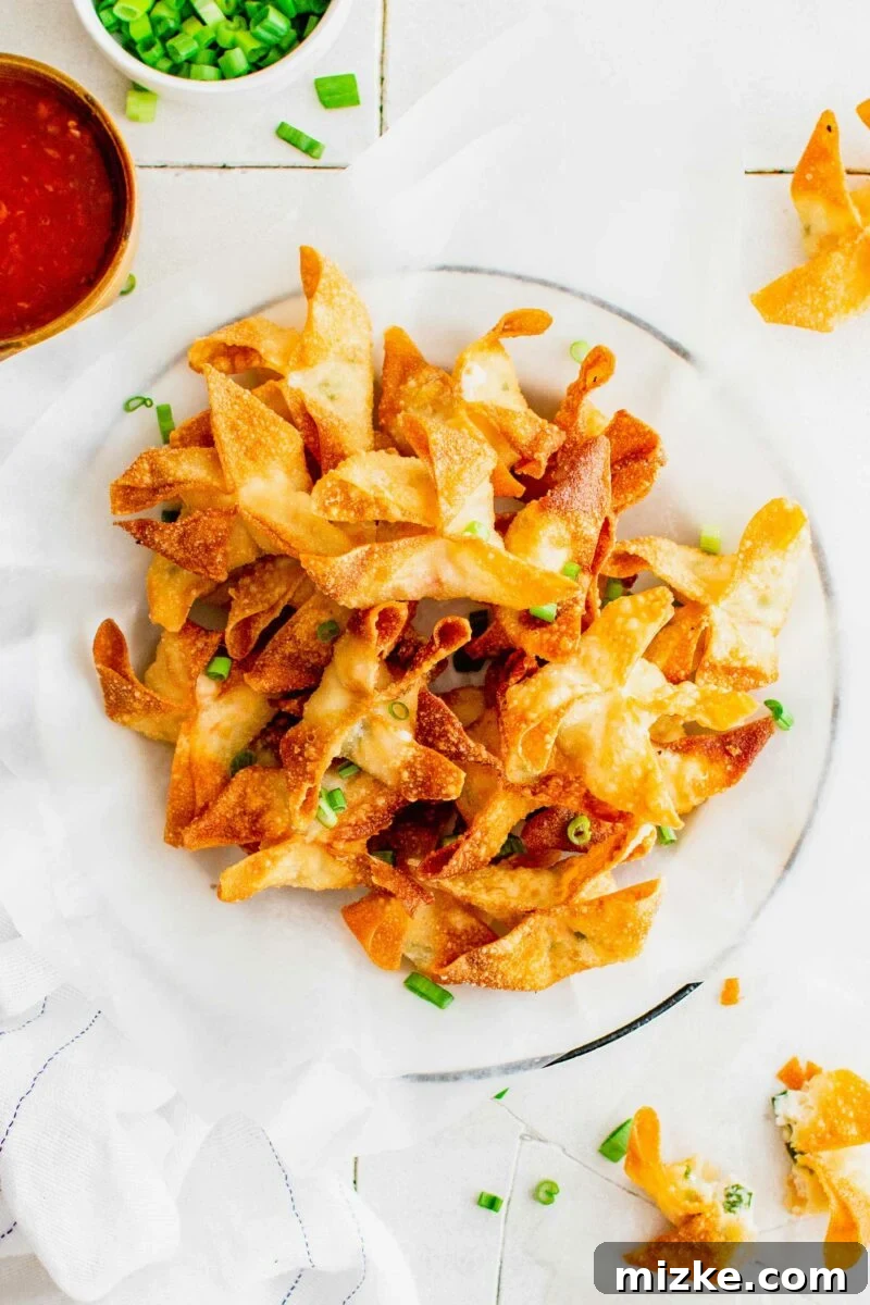 Golden Crispy Crab Bites 3 A sheet of parchment paper is topped with perfectly cooked crab rangoon and a scattering of fresh green onions, ready for serving.