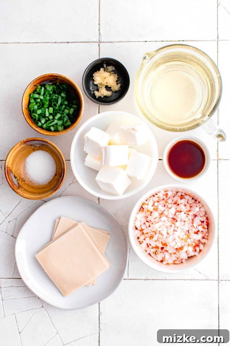 Golden Crispy Crab Bites 4 A visually appealing flat lay of fresh ingredients for making crab rangoon: minced garlic, a small bowl of oil, soy sauce, imitation crab meat, a stack of wonton wrappers, a pinch of salt, chopped scallions, and a block of cream cheese.