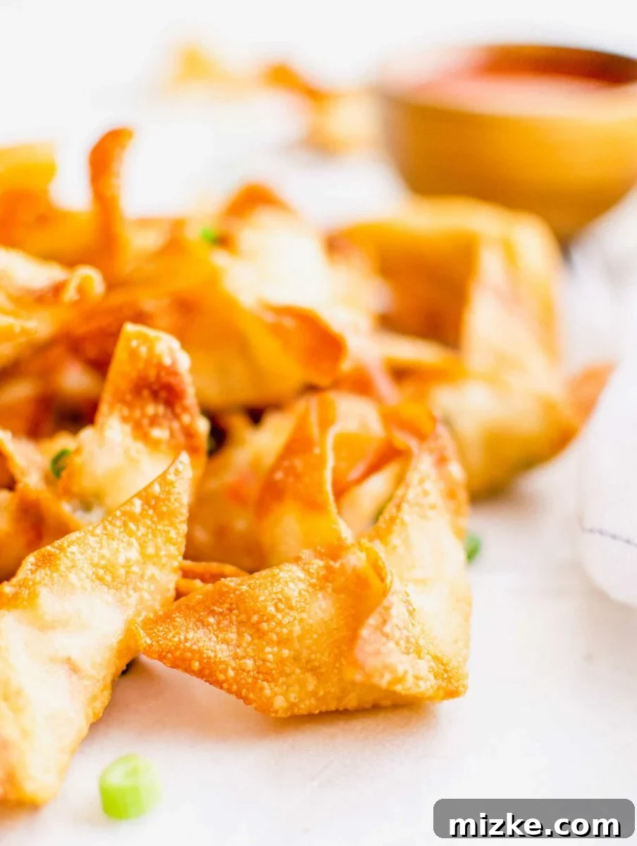 Golden Crispy Crab Bites 5 A close up image shows a golden brown, perfectly cooked crab rangoon with a slight hint of its creamy filling peeking through, highlighting its crisp texture.
