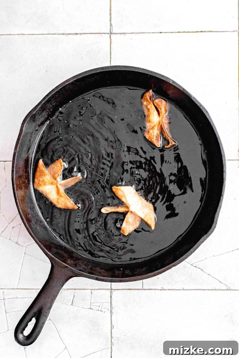 Golden Crispy Crab Bites 10 Several crab rangoon shallow frying to a golden brown in a cast iron skillet filled with hot oil, indicating the cooking process.