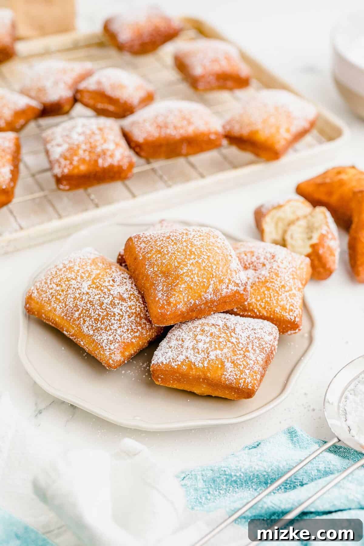 Pillowy Beignet Perfection 2 A white plate is topped with five ready to eat beignets, generously dusted with powdered sugar.