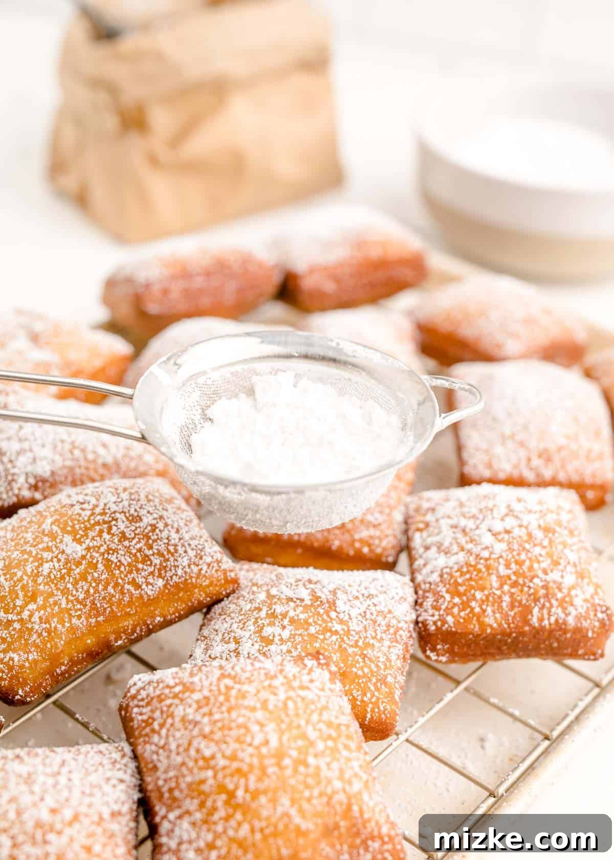 Pillowy Beignet Perfection 11 A close-up shot of dusting powdered sugar on fried beignets.
