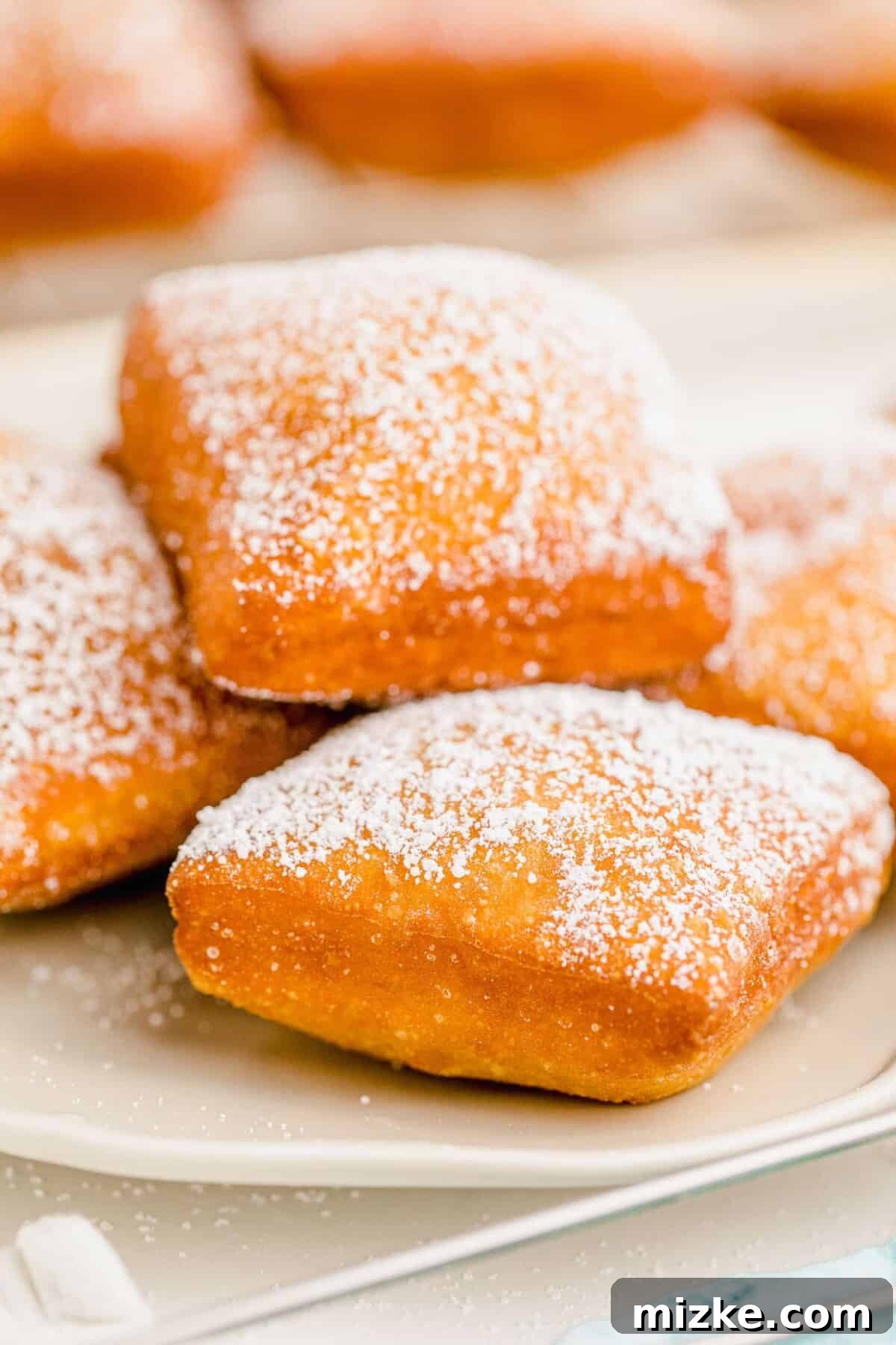 Pillowy Beignet Perfection 12 A pristine plate of beignets, perfectly dusted with white powdered sugar, ready for serving.