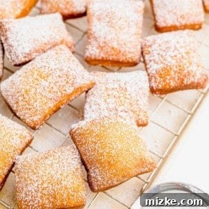 A large batch of beignets are placed on a wire cooling rack and have been dusted with powdered sugar.