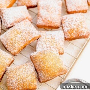 A large batch of beignets are placed on a wire cooling rack and have been dusted with powdered sugar.