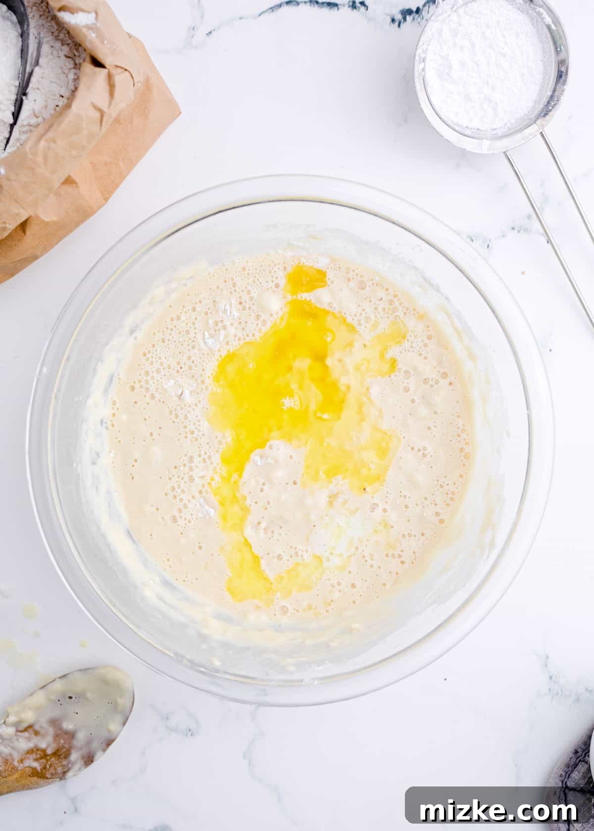 Pillowy Beignet Perfection 4 Wet ingredients for beignets being combined in a clear bowl with flour and yeast mixture.