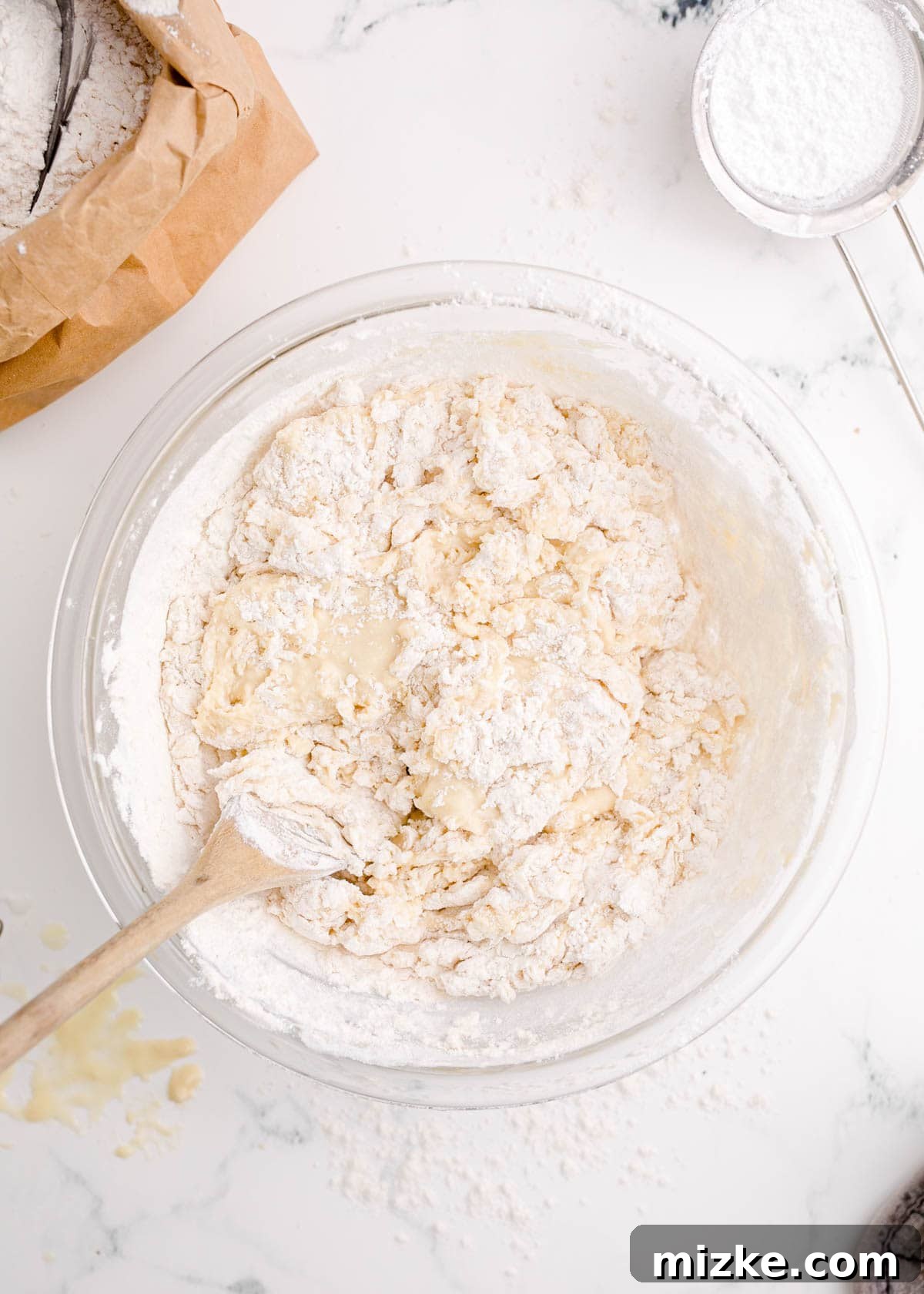 Pillowy Beignet Perfection 5 Combining the ingredients for the dough with a wooden spoon in a clear bowl.