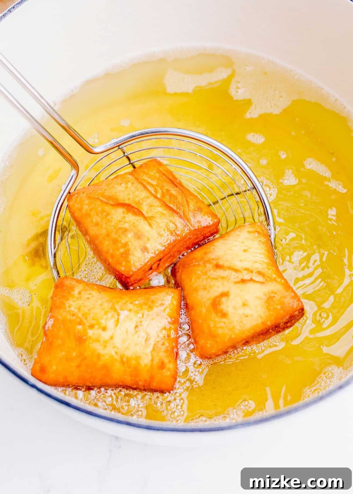 Close-up of three beignets deep-frying in a large pot filled with bubbling yellow vegetable oil.