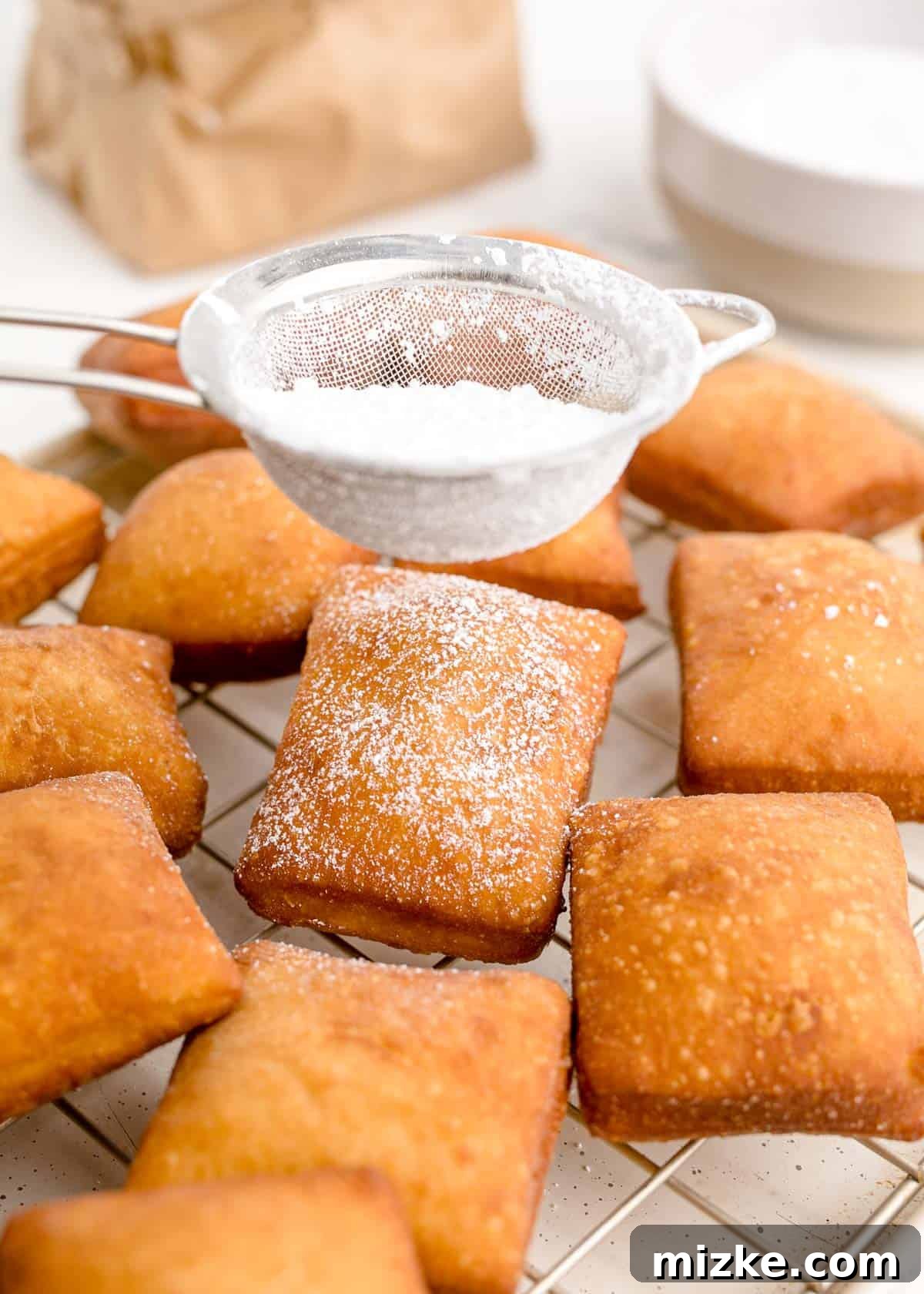 Pillowy Beignet Perfection 10 Dusting powdered sugar on fried beignets cooling on a wire rack.