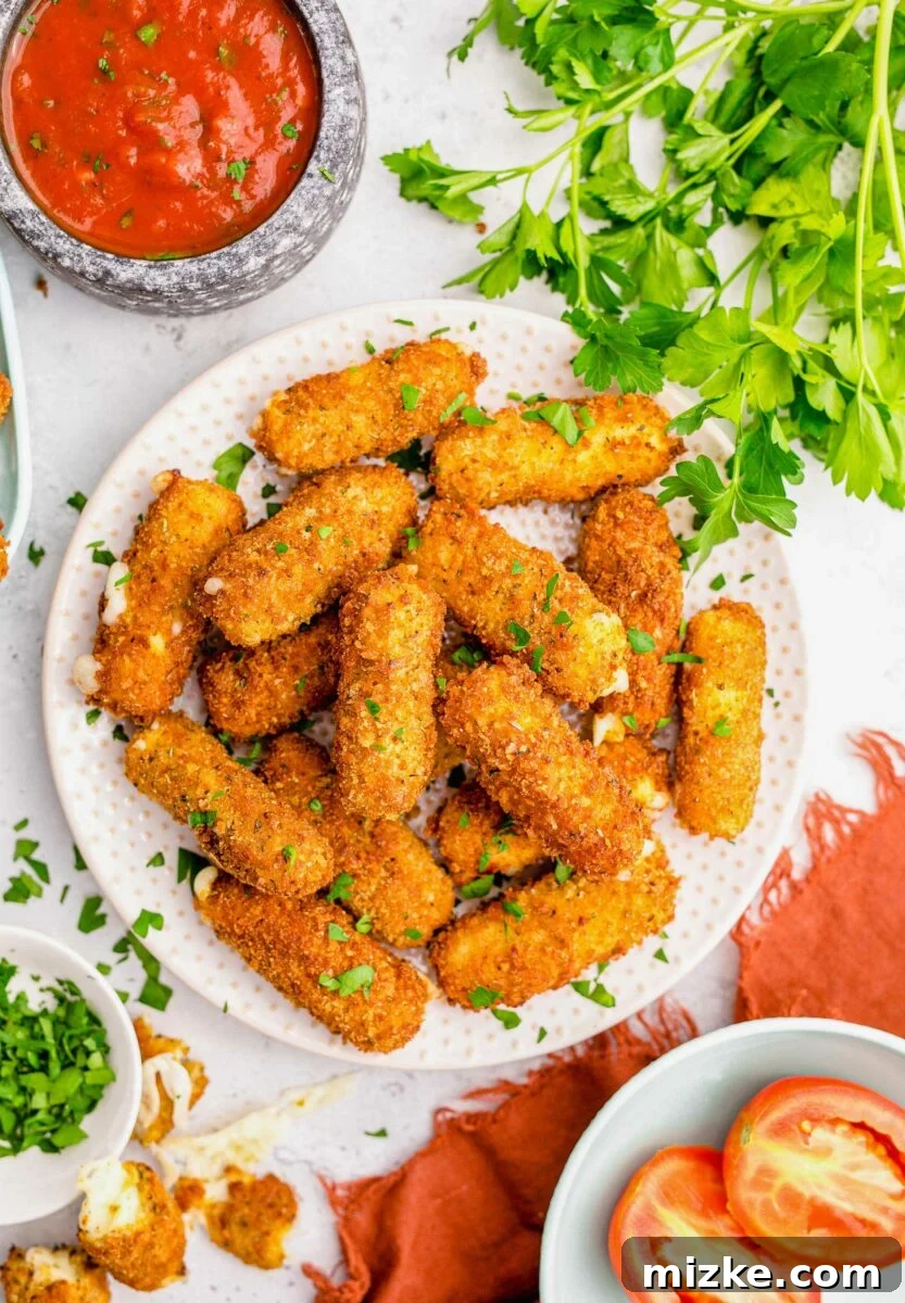 Irresistible Homemade Mozzarella Sticks 2 A round white plate filled with mozzarella stick is presented on a crowded white countertop.