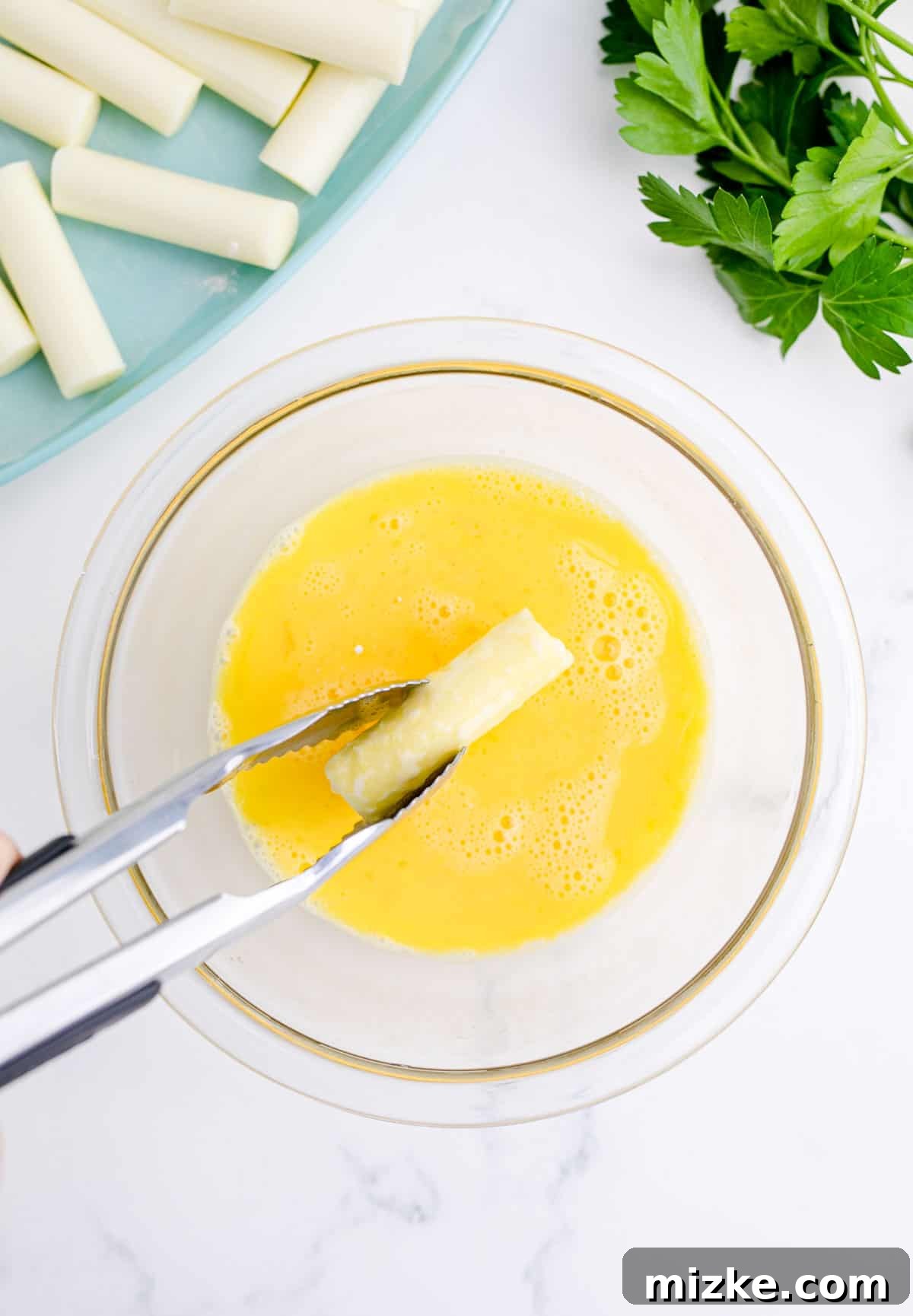 Irresistible Homemade Mozzarella Sticks 6 dipping a mozzarella stick into the egg mixture with a metal tong
