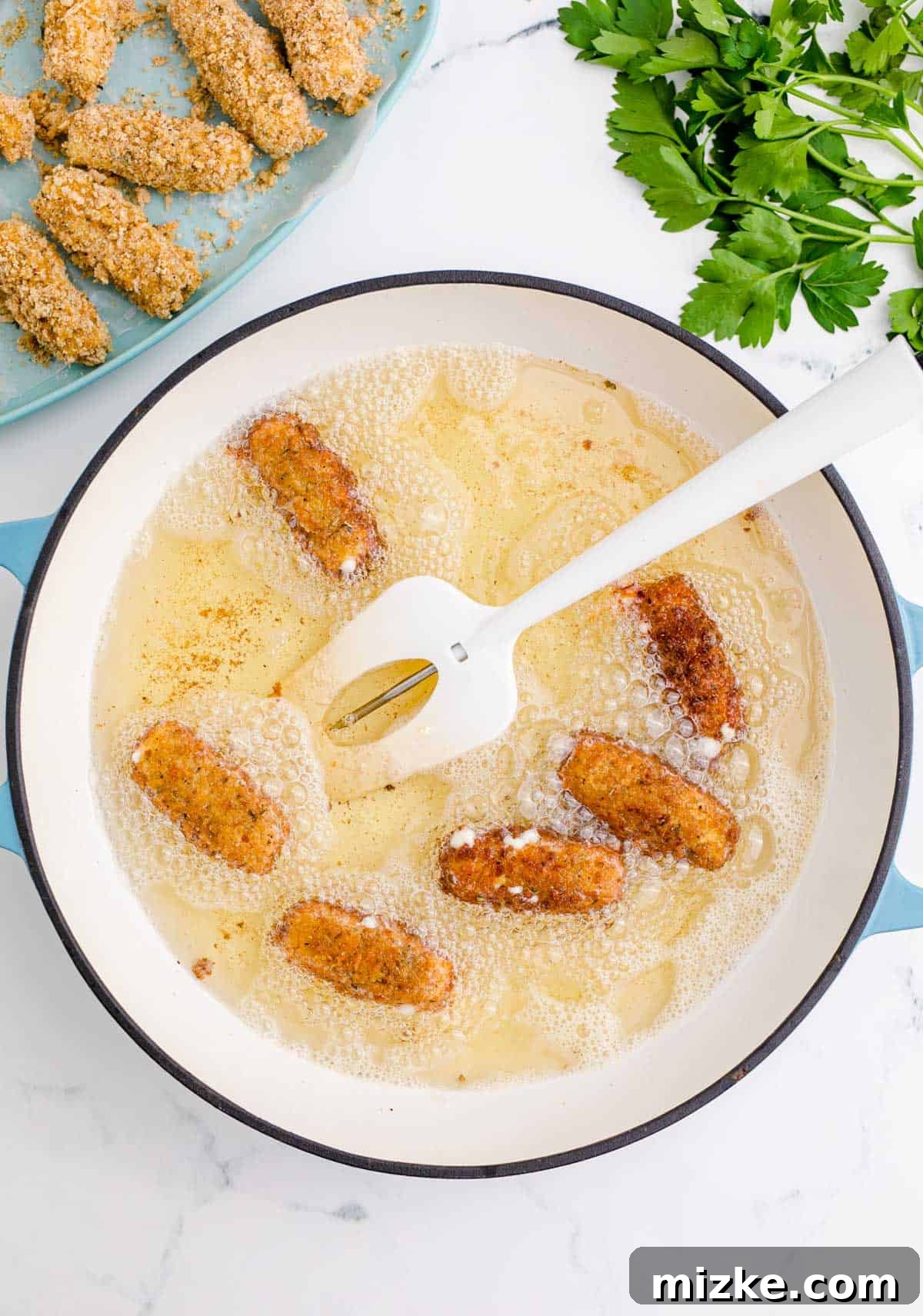 Irresistible Homemade Mozzarella Sticks 8 frying mozzarella sticks in a cast iron skillet with a white spatula and thermometer