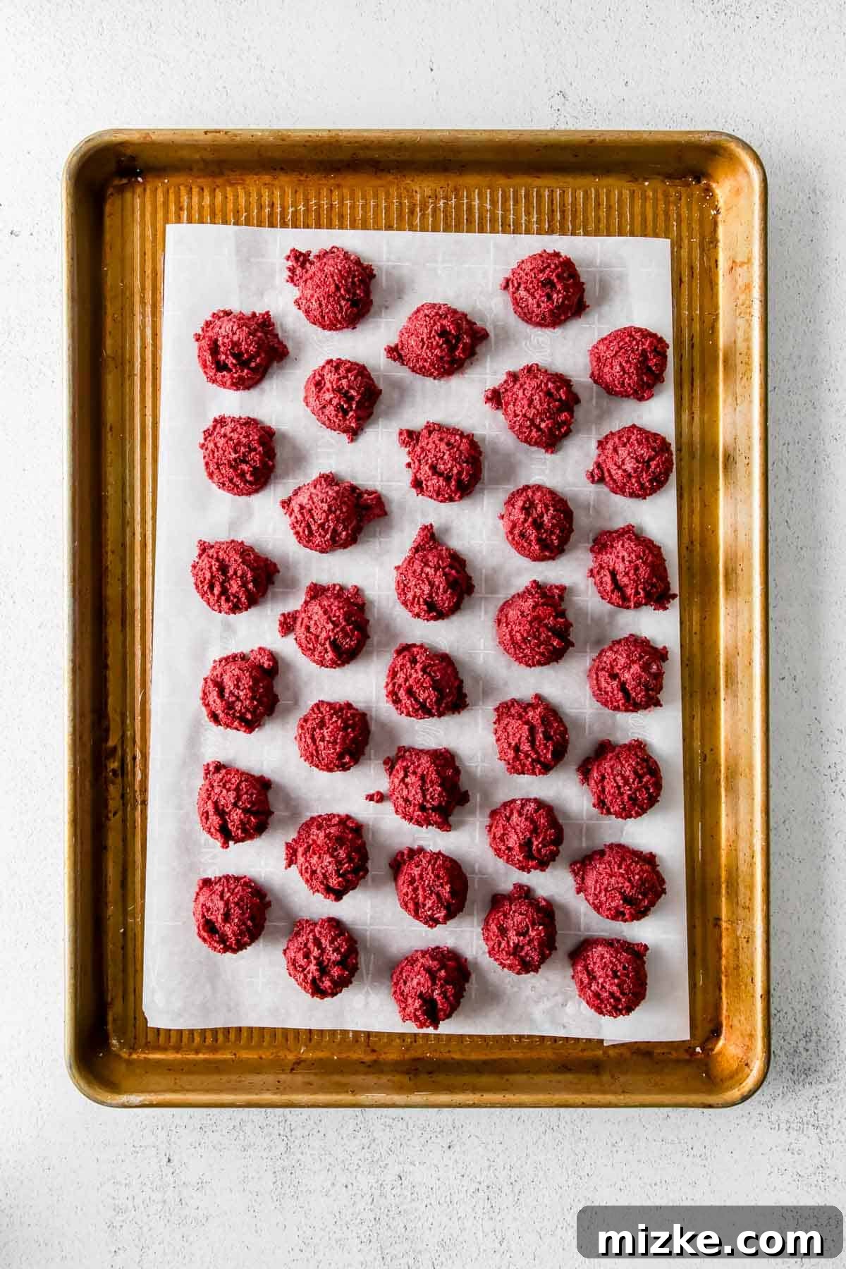 Velvet Cake Bliss Bites 4 Red velvet cake balls neatly arranged on a parchment paper lined baking sheet, ready for freezing.