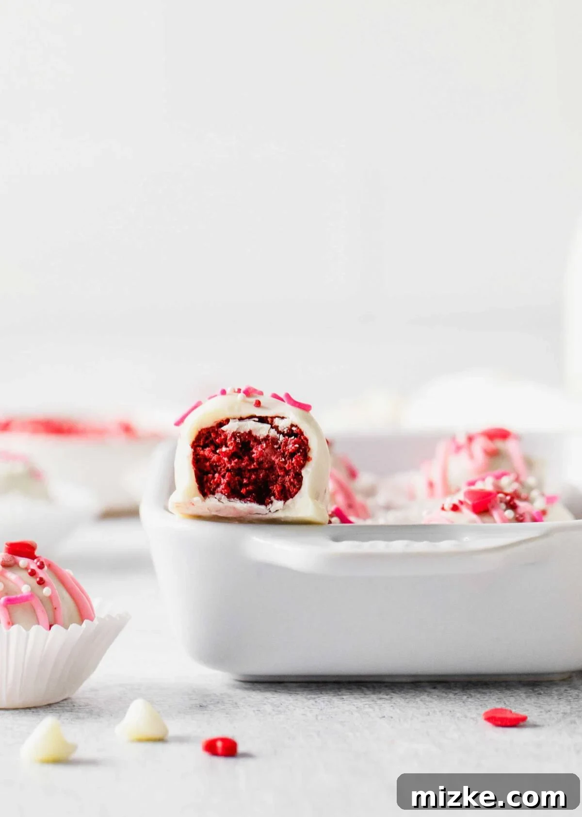 Velvet Cake Bliss Bites 5 A single red velvet cake truffle, partially eaten, resting on the edge of a baking dish, showcasing its moist interior.