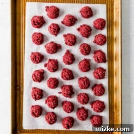 red velvet cake balls on a parchment paper lined baking sheet