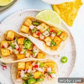 Three tofu tacos on plate with lime wedge and tortilla chips