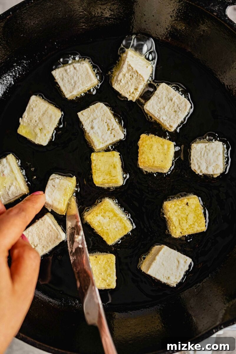 Beyond Bland: Unlock Tofu's Flavor Secrets 3 Cubes of tofu cooking in oil, sizzling in a non-stick pan