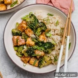Overhead view of a teriyaki tofu bowl with broccoli, with a pair of chopsticks resting on the edge of the bowl.