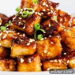 A pile of sesame garlic fried tofu on a plate garnished with sesame seeds.