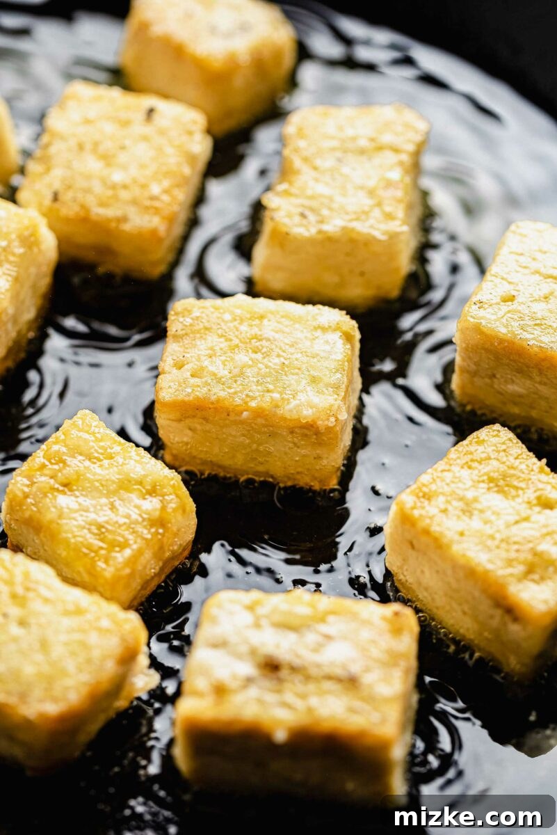 Beyond Bland: Unlock Tofu's Flavor Secrets 7 Close up of cubes of tofu frying in a hot pan, showing the golden-brown crust forming