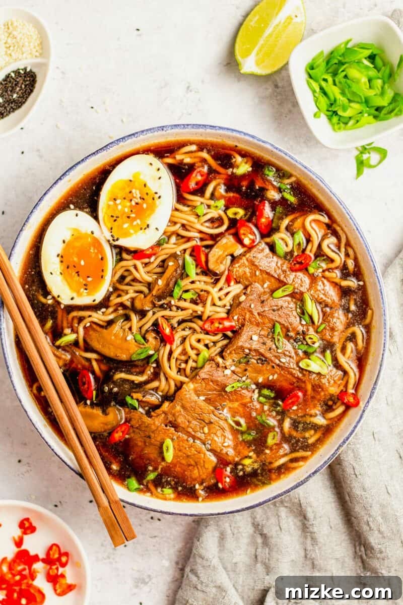 Beef Ramen Bliss 2 A steaming bowl of homemade beef ramen noodle soup, garnished with tender beef slices, perfectly soft-boiled eggs, vibrant green onions, and chopsticks resting on the rim.