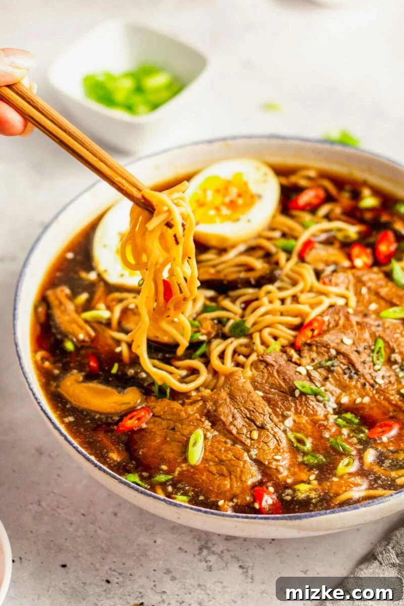 Beef Ramen Bliss 5 A pair of chopsticks gently lifts a generous portion of noodles from a delicious bowl of beef ramen noodle soup, highlighting the texture of the noodles.