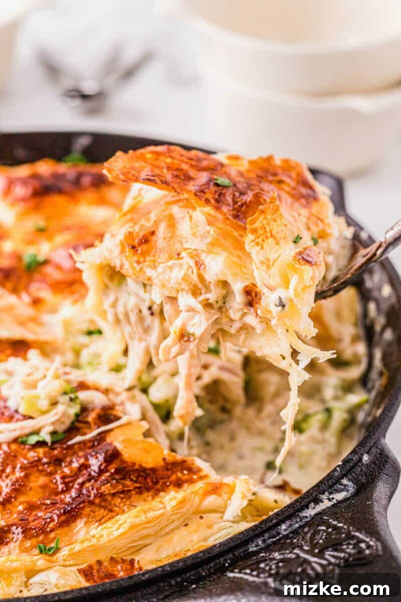 Velvety Chicken Alfredo Pot Pie 3 A serving of chicken alfredo pot pie is being lifted from the black cast iron skillet, showing the creamy filling and flaky crust.
