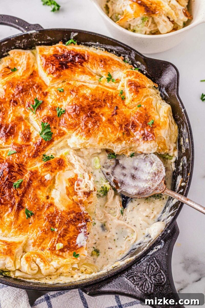Velvety Chicken Alfredo Pot Pie 4 A large serving spoon is placed in a skillet filled with cooked alfredo pot pie, showcasing its texture.